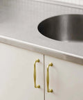 Brushed Gold Cabinet Pulls 5 Inch Hole Center 6 Pack Zinc Alloy Handles on white kitchen cabinets with stainless steel countertop.