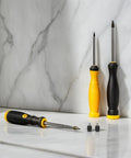 Set of two screwdrivers with black and yellow handles and two small black parts on a marble surface.