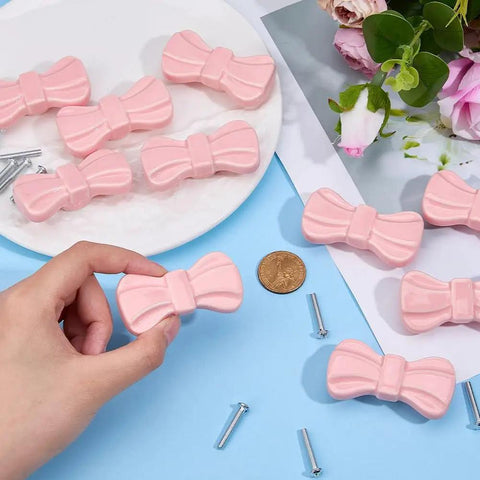 Hand holding Top Tier Pink Bow Ceramic Cabinet Knobs and Decorative Drawer Pulls with mounting screws for furniture updating.