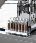 Single Dose Coffee Bean Storage Tubes, Glass And Aluminum Vials, Fourteen Piece Set With Acrylic Board displayed on espresso machine.