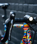 USB Rechargeable Bike Light With 250 Lumen Front Headlight mounted on a colorful bike against a brick wall.