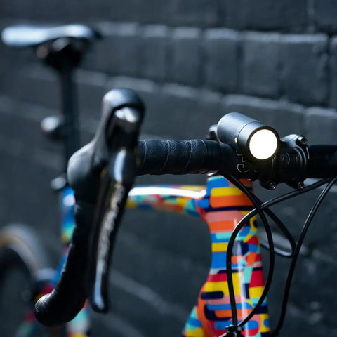 USB Rechargeable Bike Light With 250 Lumen Front Headlight mounted on a colorful bike against a brick wall.
