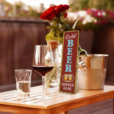 Rustic Cold Beer Served Here Metal Wall Sign Retro Vertical Tin Decor displayed on a wooden table with drinks and flowers.