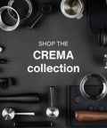 Assorted CREMA collection coffee tools including espresso tamper, rings, and frothing pitcher on a dark background.