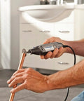 Hands using Heavy Duty 130 Watt Rotary Multi Tool Powerhouse on copper pipe for precision cutting in a home workshop.
