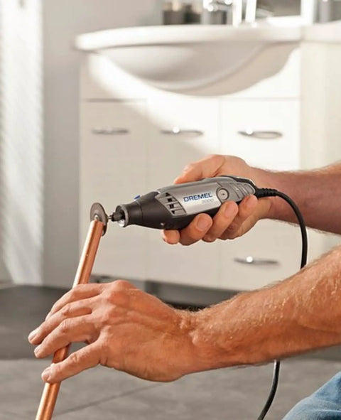 Hands using Heavy Duty 130 Watt Rotary Multi Tool Powerhouse on copper pipe for precision cutting in a home workshop.