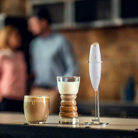 Handheld Milk Frother And Electric Whisk With 19000 RPM Power Includes Recipe Book And Stainless Steel Stand White And Gold Finish Perfect For Lattes Cappuccinos And More displayed with coffee drinks