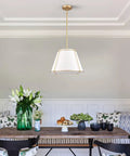 3 Light Gold Pendant Light Featuring White Linen Cone Shade And Sturdy Metal Cage drops down over a wooden dining table.