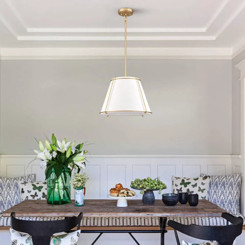 3 Light Gold Pendant Light Featuring White Linen Cone Shade And Sturdy Metal Cage drops down over a wooden dining table.