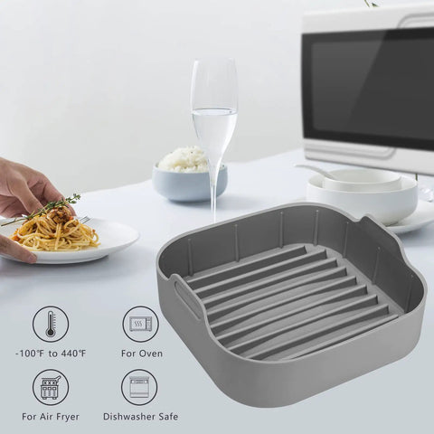 Grey air fryer silicone pot 8.1 inch basket pan with dual handles for 6.5 Qt square fryers next to a pasta plate on a table.