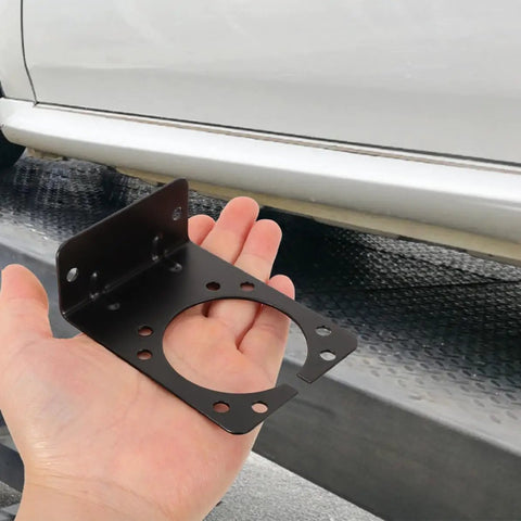 2 Pack Pin Trailer Wiring Connector Mounting Brackets For 7 Way RV Socket And Vehicle Trailer Plug, Heavy Duty Iron Mounts With Easy Install No Fuss, Rock Solid Power Transmission, Compatible For Secure Towing black iron bracket with hand, shown beside vehicle for 7-way RV socket