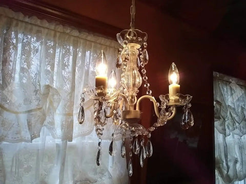 Plug In Crystal Swag Chandelier With Three Lights, White Metal Frame, Clear Glass Stem And Acrylic Crystals glowing indoors