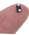 Heavy Duty US1K 1A 800V Rectifier Diodes 100 Pack on fingertip, small SMD diodes for electronics, 5mm x 2mm size.