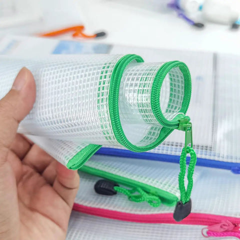 Close-up of a hand holding a clear mesh zipper pouch with a green trim, part of a 24 Pack Small Mesh Zipper Pouches With Label Pocket Waterproof Bags For School Office Supplies Cosmetics And Travel Essentials 6.3 By 4.9 Inches Clear See Through Organizers For Gear.