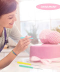 User decorating a pink cake with Hella Sharp Icing Scribe Tool Kit With 12 Stainless Steel Fondant Needles for intricate designs.