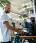 Person using an Electric Automatic Espresso Tamper For Home Baristas Featuring Self Leveling Precision With A Tight 53mm Fit providing coffee.