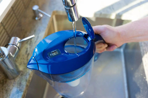 Filling a blue water pitcher with Pure Replacement Filter For Water Pitcher That Removes Fluoride Lead Forever Chemicals Heavy Metals And Industrial Pollutants Delivers Clean Great Tasting Water 100 Gallon Capacity Easy Swap attached.