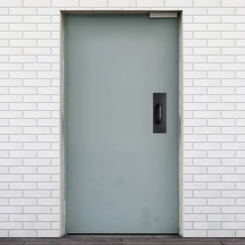 Black Stainless Steel Door Handle Pull Plate for Commercial Doors installed on a gray door in a brick wall