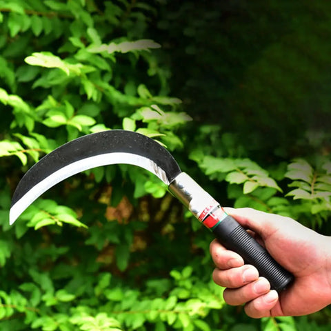 Hand holding Two Pack Manganese Steel Weeding Sickle Set For Easy Yard Work, Weed Cutting And Harvesting in front of green foliage.