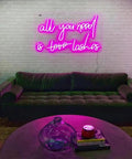 Pink 'All You Need Is Love Lashes' neon sign above a green couch in a living room setting