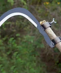 Durable Manganese Steel Blade Sickle With Replaceable Wooden Handle, mounted on wooden stick, in garden setting, side view