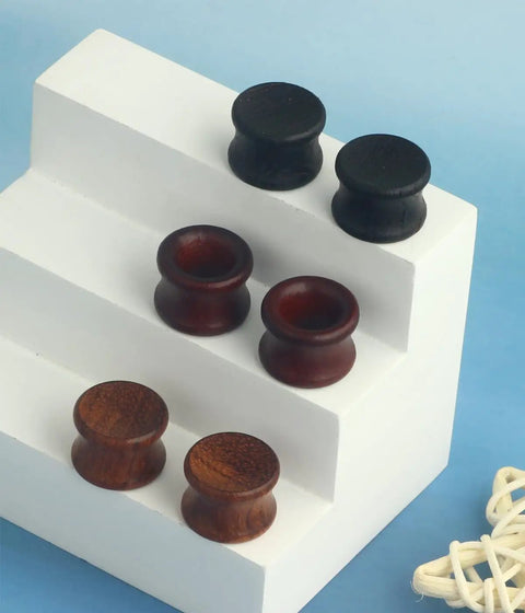 Three Pairs Organic Wood Ear Plugs Set With Double Flared Ear Tunnels Saddle Fit Wooden Gauges Five Eighths Inch 16mm Natural Black Brown Tones Perfect For Punk Piercing And Everyday Wear displayed on a white stand