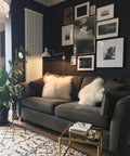 Living room with dark walls, wall art, and a dark gray sofa decorated with fluffy white pillows, plant in a corner