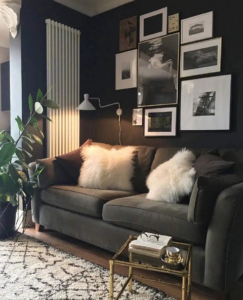 Living room with dark walls, wall art, and a dark gray sofa decorated with fluffy white pillows, plant in a corner