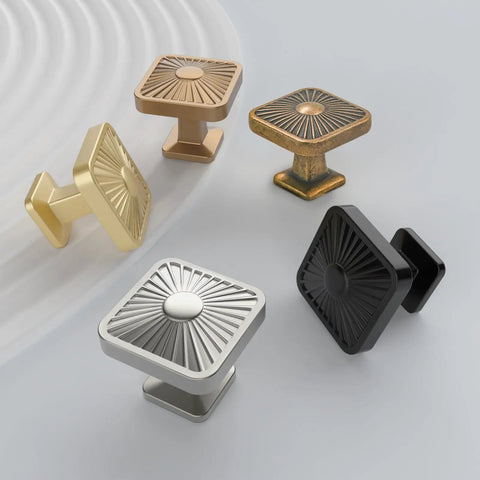 Set of five diverse style square cabinet knobs in brushed gold, silver, and black finishes on a light surface
