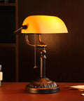 Amber Glass Bankers Desk Lamp With Retro Weighted Base And Old School Vibe on wooden desk, pull chain visible