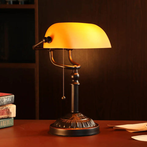 Amber Glass Bankers Desk Lamp With Retro Weighted Base And Old School Vibe on wooden desk, pull chain visible