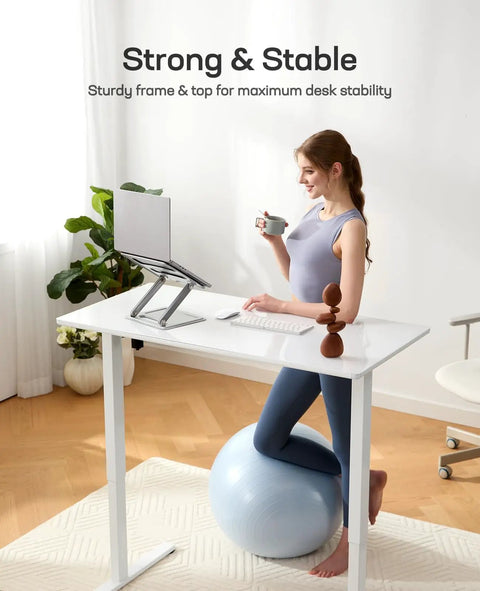 Person sitting on exercise ball at Glass Standing Desk With Drawer 37 X 22 Inches Adjustable Height With Four Preset Levels One Piece Tempered Glass Top White Ergonomic Home Office Desk For Standing Work.