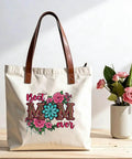 Canvas bag with floral 'Best Mom Ever' print, featuring pink and teal flowers, sitting next to a vase of roses. Four Pack Iron On Transfers For T Shirts DTF Ready To Press Easy To Apply With Any Home Iron Or Heat Press Floral Mama Leopard Print Designs For Clothes Pillows Bags And DIY Crafts Assorted Sizes.