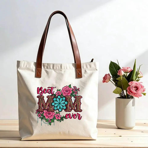 Canvas bag with floral 'Best Mom Ever' print, featuring pink and teal flowers, sitting next to a vase of roses. Four Pack Iron On Transfers For T Shirts DTF Ready To Press Easy To Apply With Any Home Iron Or Heat Press Floral Mama Leopard Print Designs For Clothes Pillows Bags And DIY Crafts Assorted Sizes.