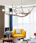 Modern Glass Bubble Chandelier With Sleek Wood Branch Accents, Rustic Industrial Flush Mount Pendant Light For Living Room, Adjustable Hanging Lamp serving over a yellow armchair.