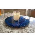 Ocean Resin And Wood Fifteen Inch Lazy Susan With Handcrafted Wave Pattern For Kitchens And Dining Tables Smooth 360 Degree Rotation Serving Tray And Charcuterie Board A Unique Centerpiece And Gift Idea with a glass of milk on top on a marble countertop.
