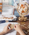LED Illuminated 3D Wooden Globe Puzzle For Adults With Stand Build Your Own Night Light World Globe Kit 180 Pre-Cut Pieces Educational Decor Gift For Birthday Or Anniversary, hands assembling wooden globe parts on desk