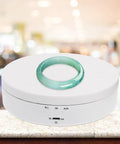 Romisbaba Electric Rotating Jewelry Display Stand For Bracelets Watches With Motorized Turntable And Cool LED Lighting showcasing a jade ring on a white base.
