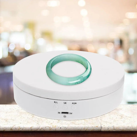 Romisbaba Electric Rotating Jewelry Display Stand For Bracelets Watches With Motorized Turntable And Cool LED Lighting showcasing a jade ring on a white base.