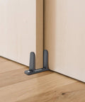 4-Piece Black Closet Door Floor Guide Set With Screws And Screwdriver For Smooth Sliding Closet Doors Fits 1-3/8 Inch Thick Doors Includes Floor Guides, Durable Hardware For Easy Installation installed under a wooden door.