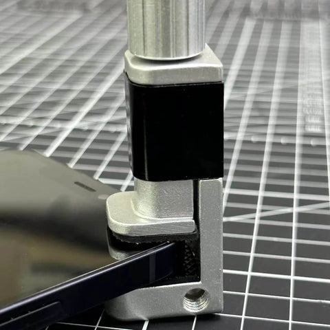 Close-up of adjustable screen repair clamps kit for phones and tablets holding a device screen securely on a grid surface.