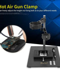 Sturdy Adjustable Hot Air Gun Holder With Cast Aluminum Base Clamp And Two Fixtures For BGA Rework Soldering Station Flexible Desktop Mount For Hands Free Soldering with black design and tool slots, close-up view of circuit board.