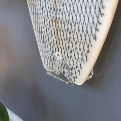 Close-up of Heavy Duty Vertical Surfboard Wall Mount Rack Made From Crystal Clear Acrylic holding a surfboard against a wall.