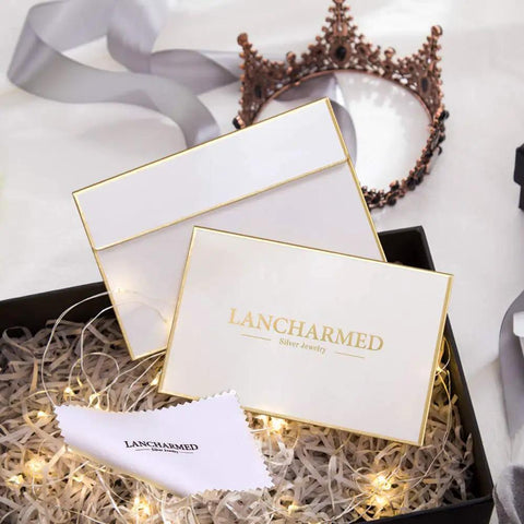 Gift box with Lancharmed Silver Jewelry branding, featuring decorative lights and a crown in the background.