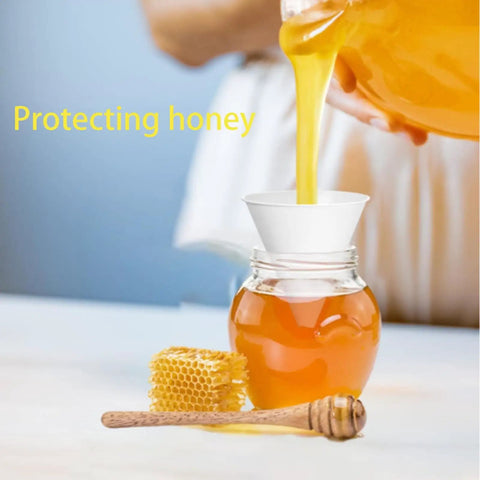 Glass jar with honey poured through a paper funnel into the jar, hexagonal honeycomb and dipper nearby.