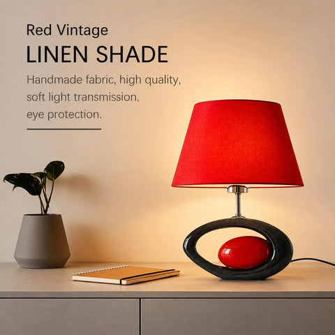 Red Modern Table Lamp With Ceramic Body And Linen Shade on desk, glowing softly, next to plant and notepad