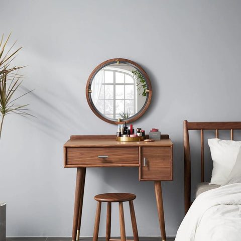 Modern wooden vanity with round mirror and stool, next to a bed in a minimalist bedroom, against grey wall.