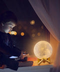 Child reading by Moon Lamp 7 Inch 3D Printed Moon Light With Stand, 16 Color LED Night Light on windowsill