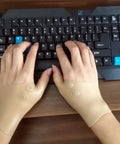 Hands wearing Thumb And Wrist Support Brace 2 Pack With Elastic Gel Fingerless Glove typing on keyboard for pain relief and wrist support