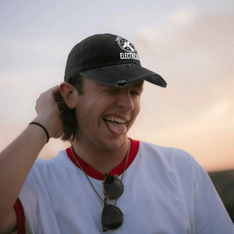 Young man wearing Trust Me I Am An Electrician Hat With Laser Engraved Design, adjustable trucker cap, outdoor setting.